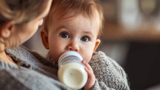 bebé tomando un biberón de leche en brazos de su madre, en un ambiente cálido y acogedor.
