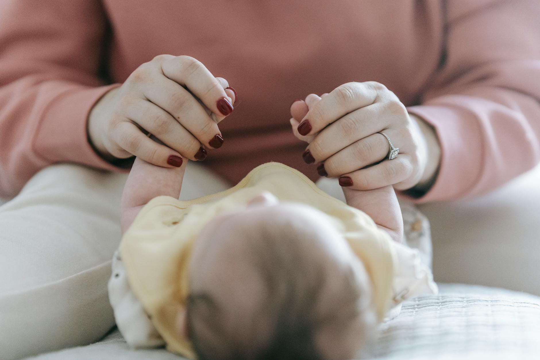 crop unrecognizable mother holding hands of newborn baby on bed