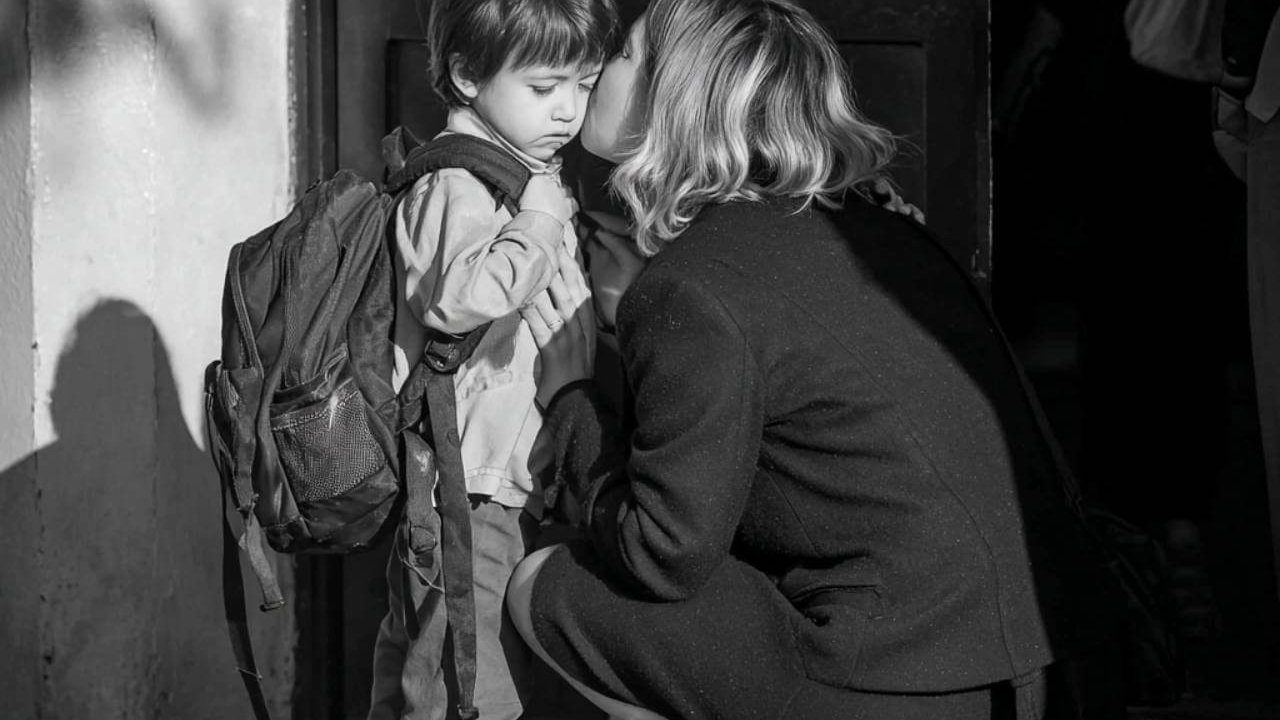 Madre despide y consuela a su hijo con mochila en la puerta del colegio mientras el niño muestra tristeza.