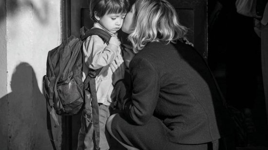 Madre despide y consuela a su hijo con mochila en la puerta del colegio mientras el niño muestra tristeza.