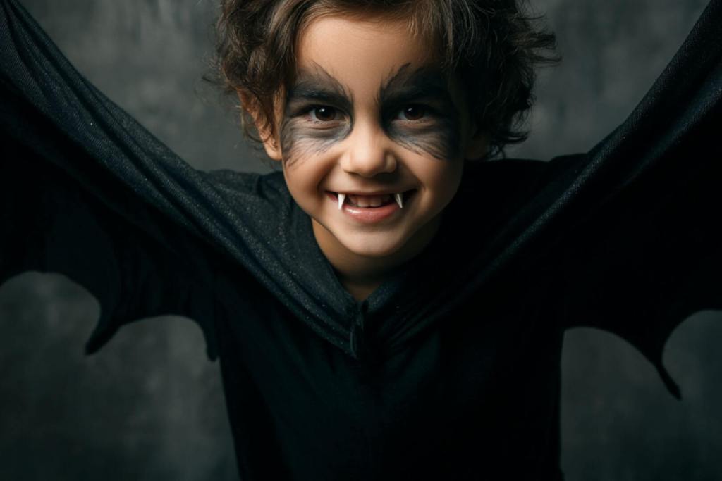 Niño disfrazado de murciélago con alas y maquillaje negro alrededor de los ojos.