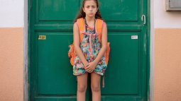 Niña con mochila escolar frente a una puerta verde antes de ir al colegio sola.