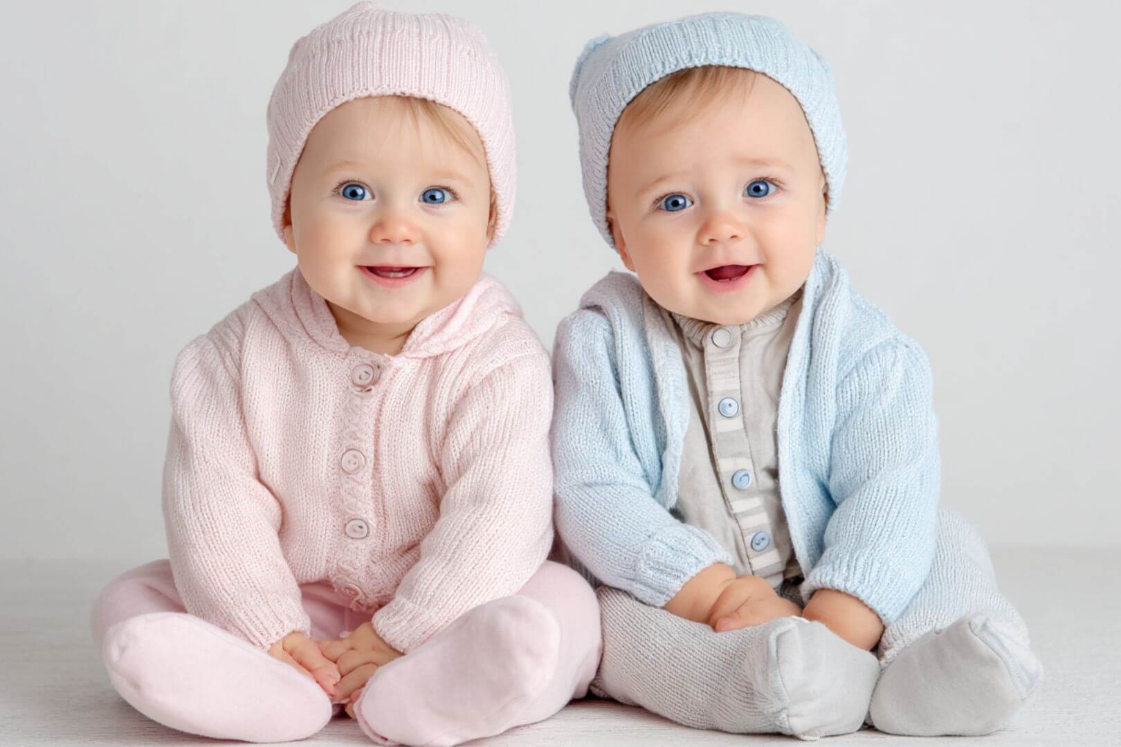 Bebé niña y bebé niño sentados juntos con ropa de punto rosa y azul