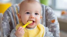 Bebé con babero amarillo comiendo puré con cuchara amarilla