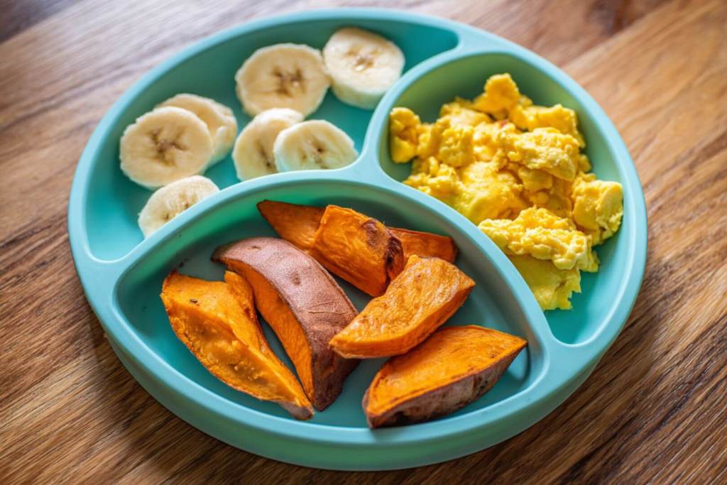 Plato infantil con boniato asado, rodajas de plátano y huevo revuelto.