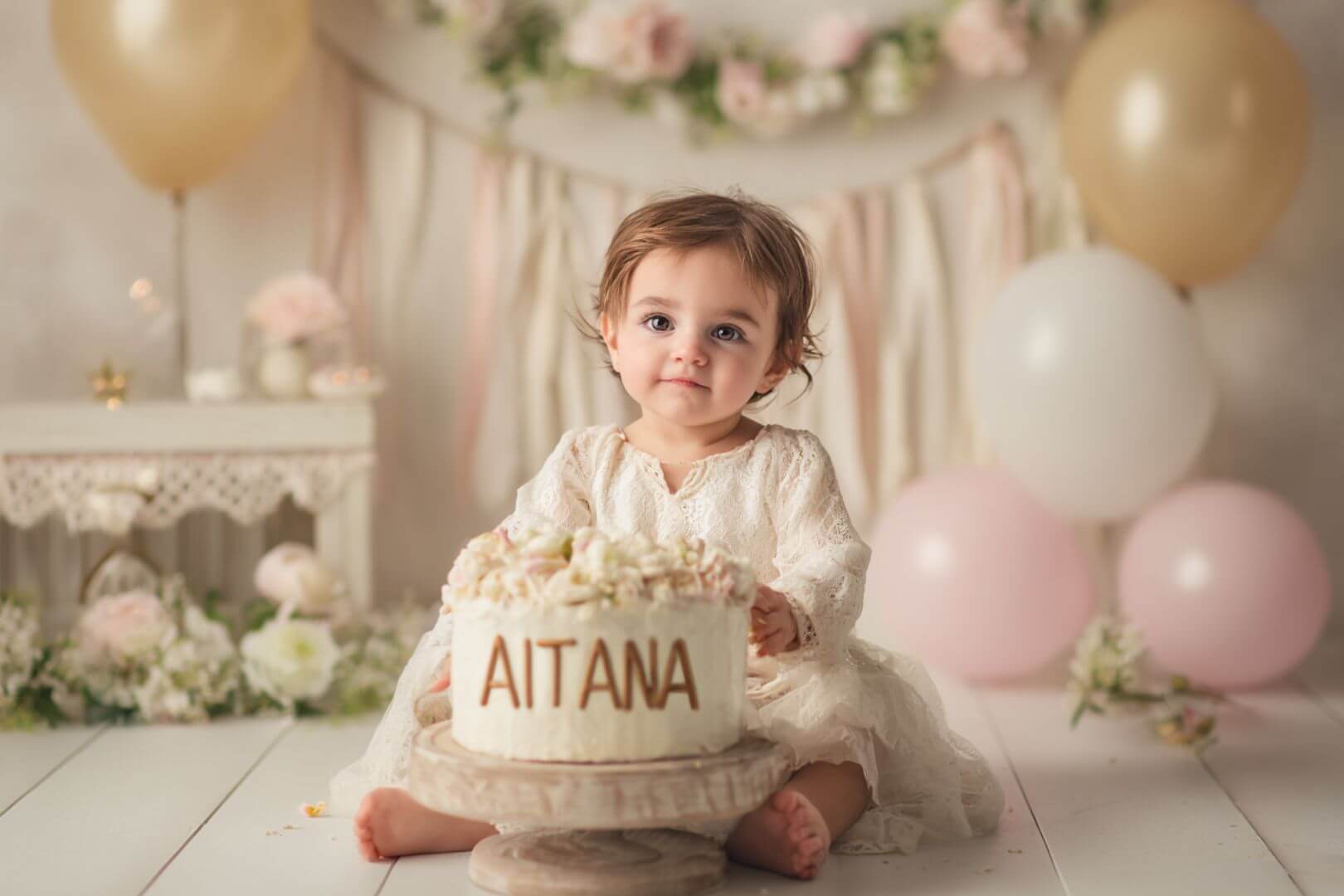 Bebé niña con expresión tierna en un entorno cálido y natural, acompañada de detalles decorativos con el nombre Aitana