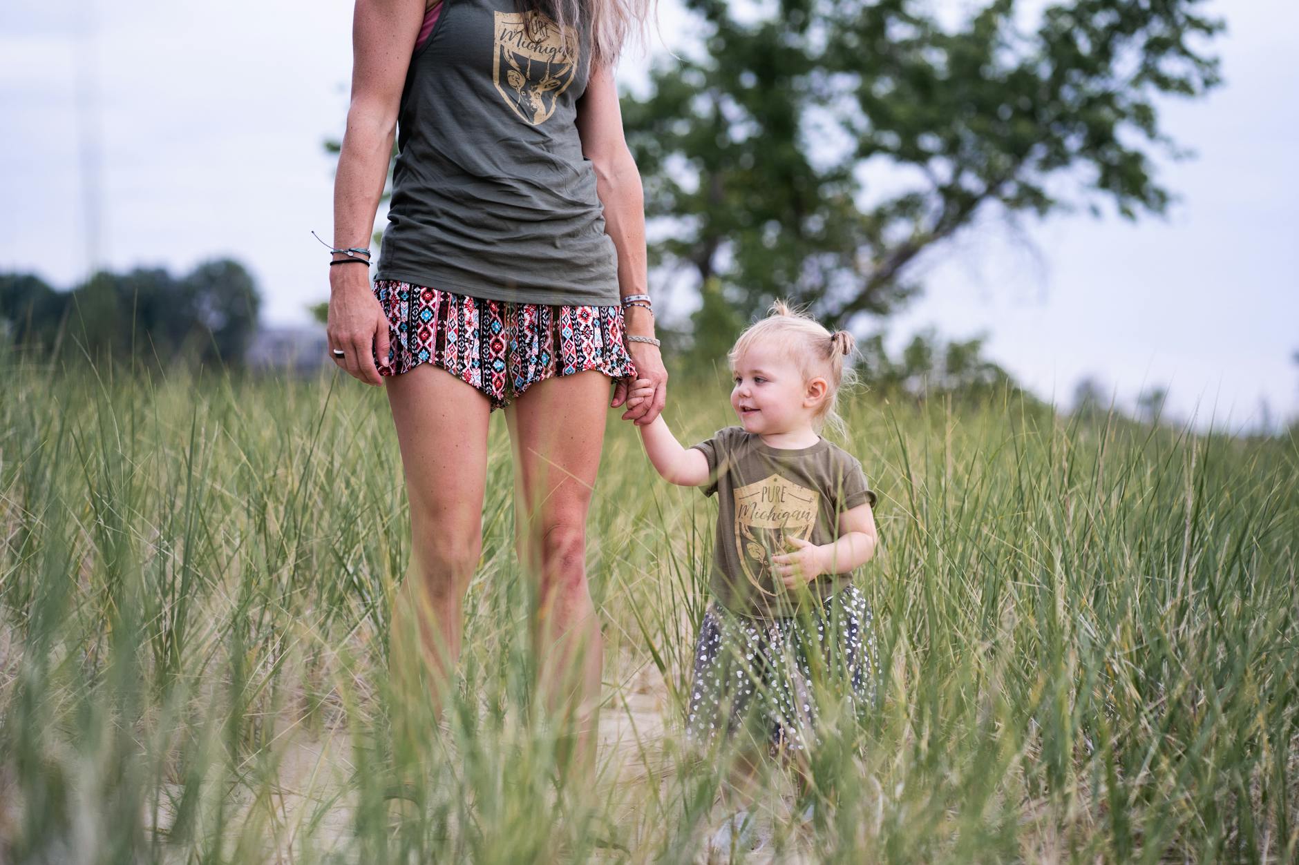 woman standing and holding hand of baby near green field