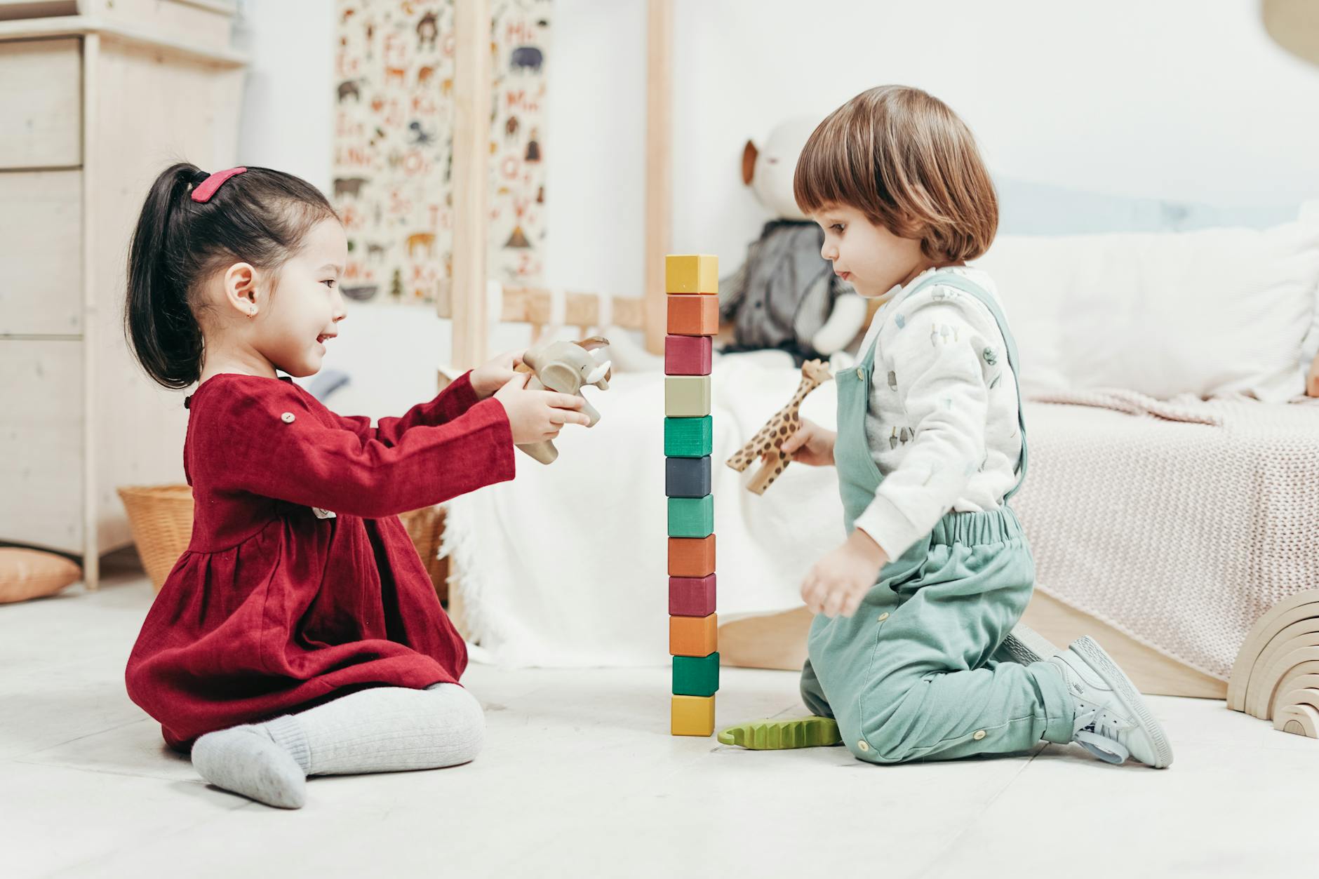boy in white long sleeve shirt and green pants sitting on floor beside girl in red