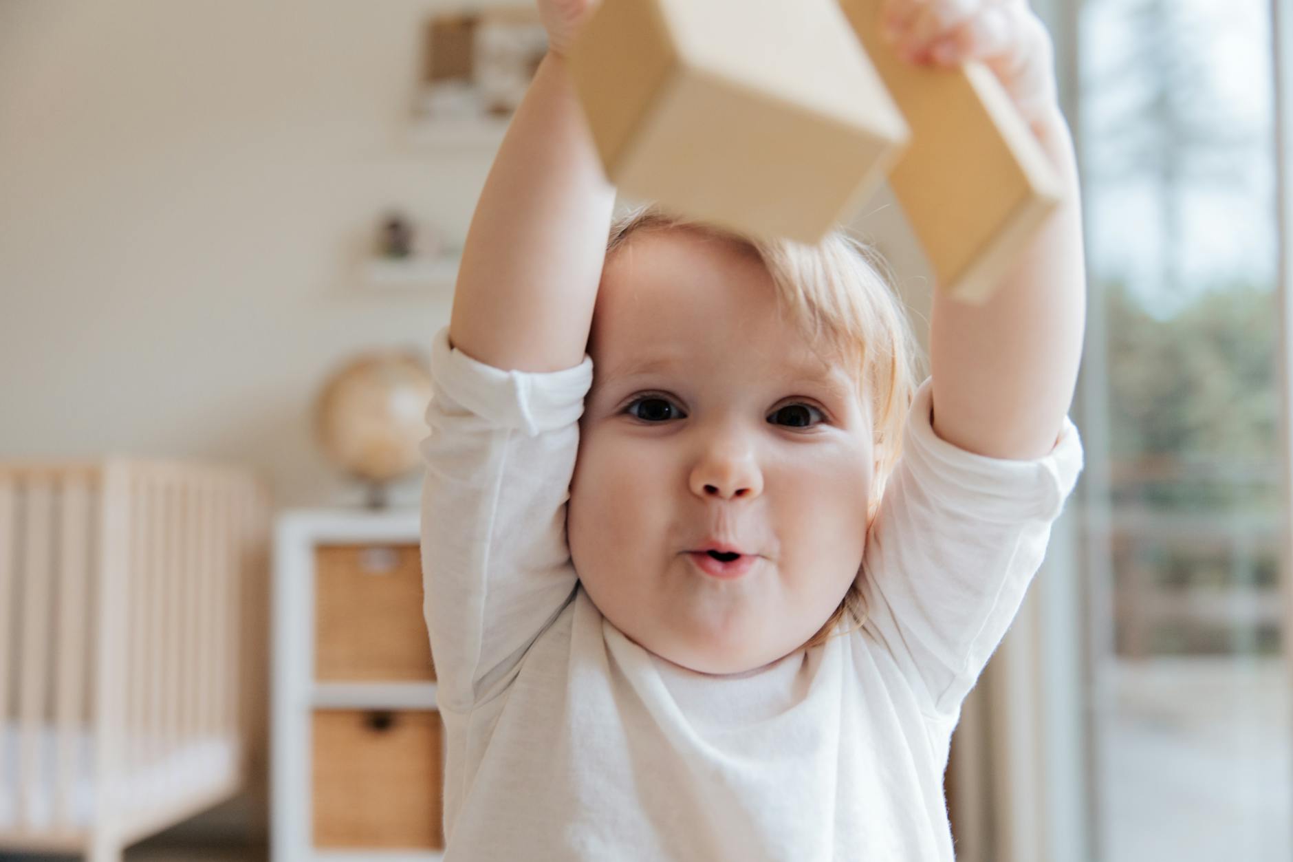baby in white onesie holding wooden blocks
