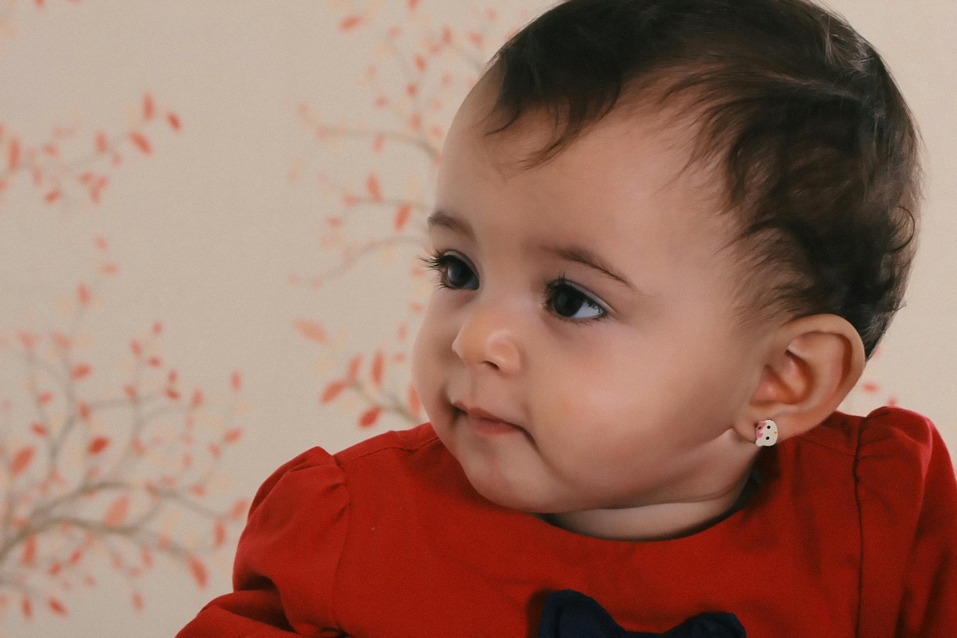 baby wearing red crew neck shirt near pink and black floral surface