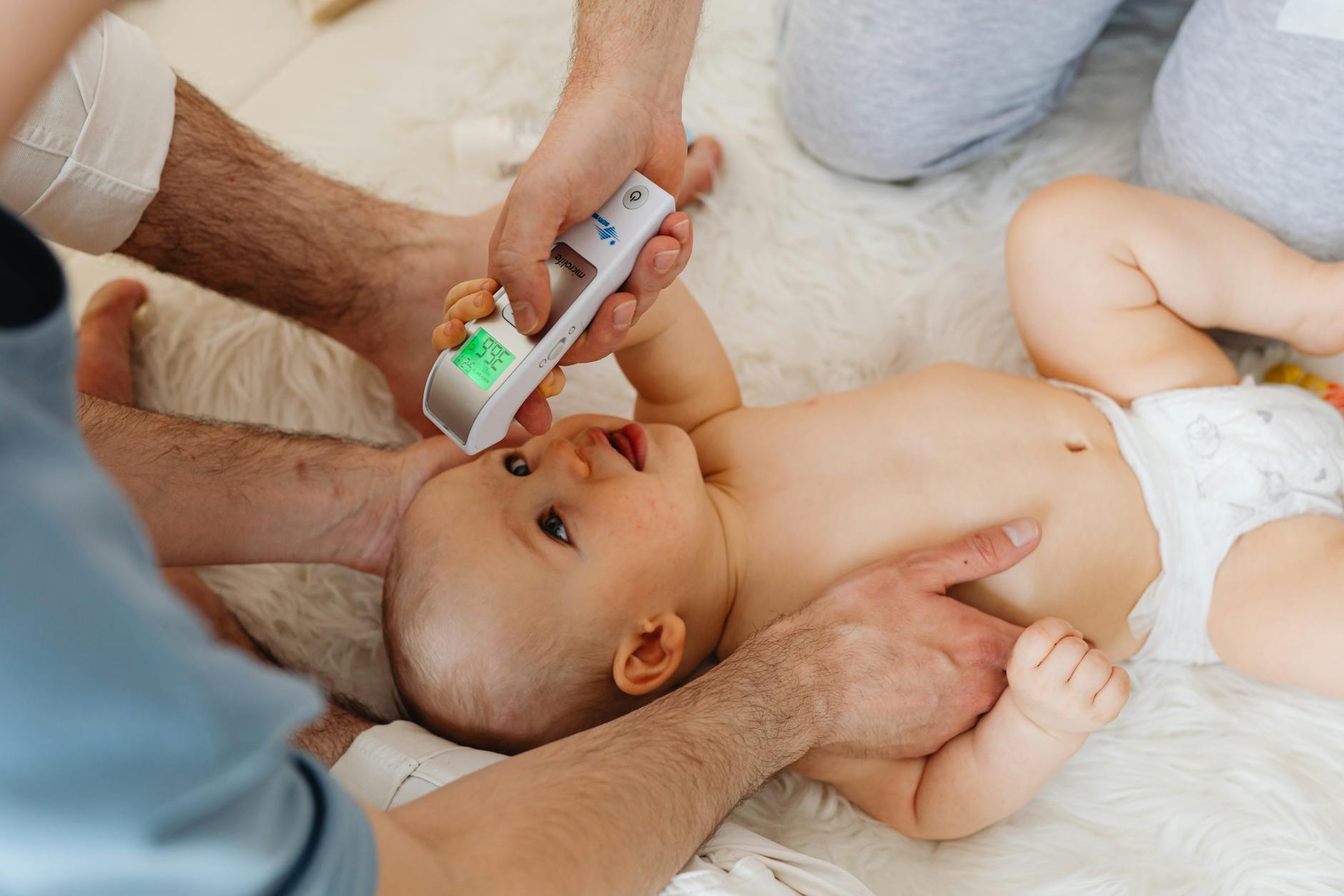 hand of a person holding a thermometer on a baby lying on white textile