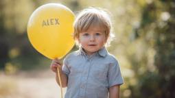 Niño pequeño sosteniendo un globo amarillo con el nombre ÁLEX al aire libre.