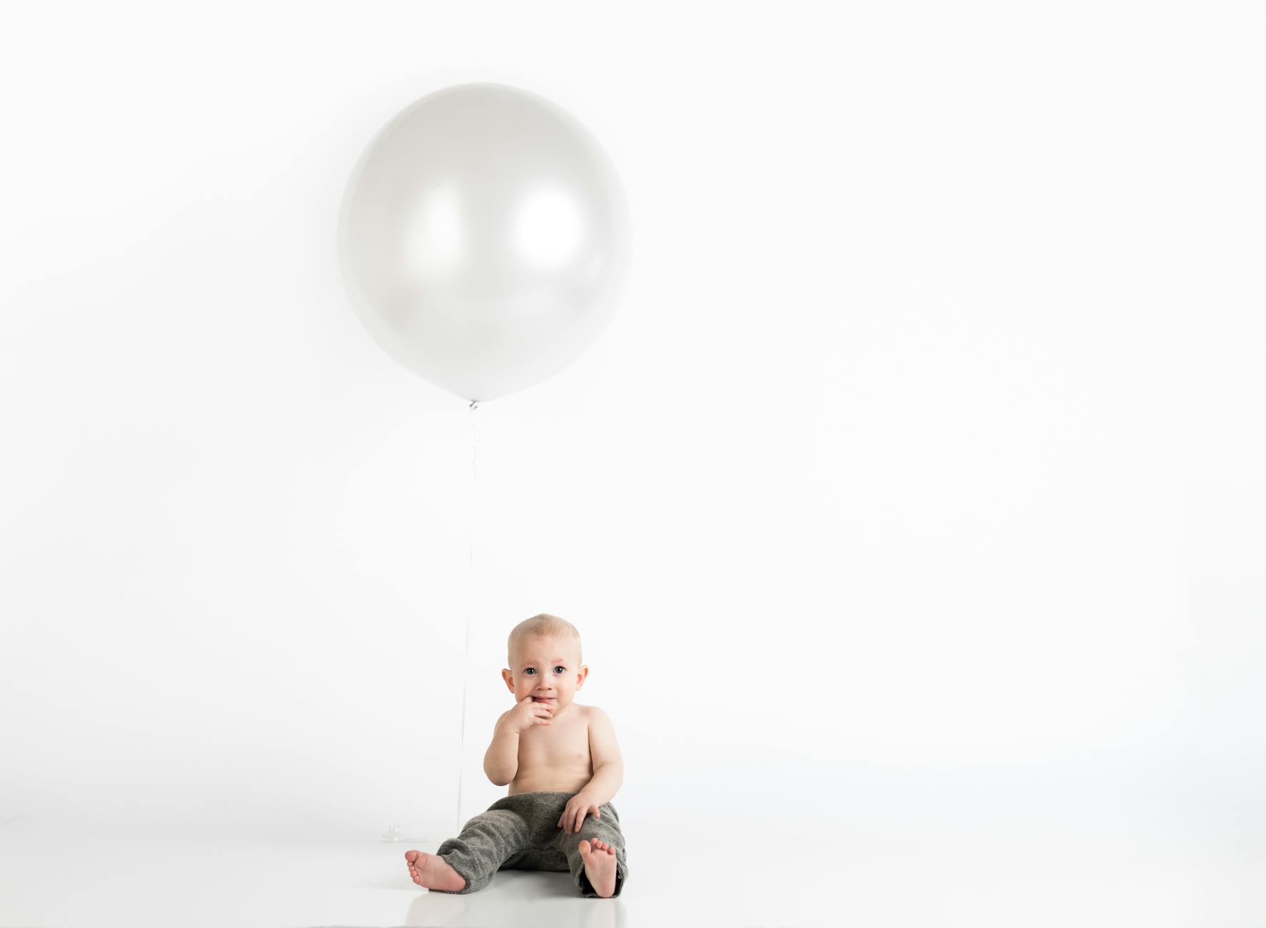 baby boy sitting with white inflatable balloon above
