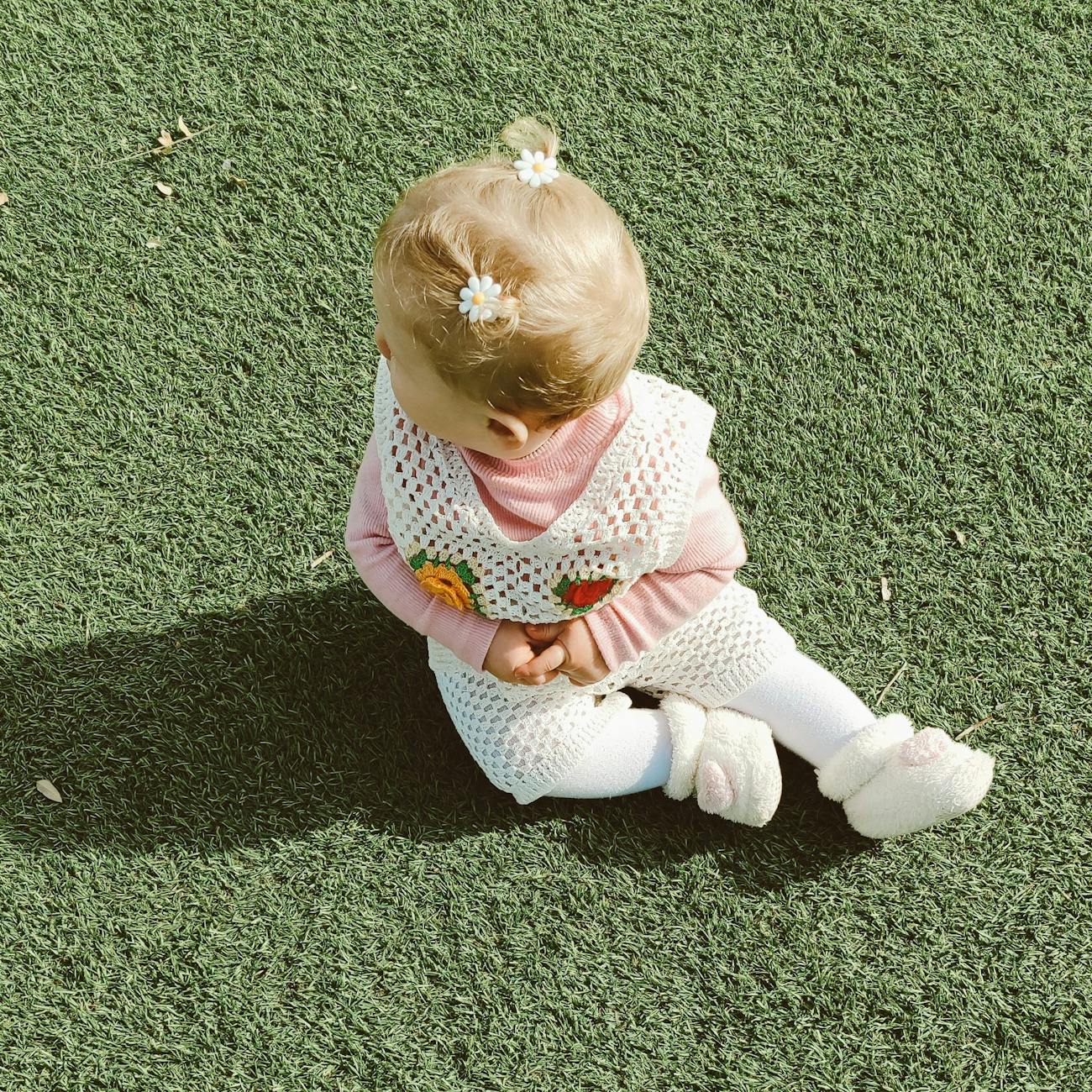 adorable baby girl sitting on green grass outdoors