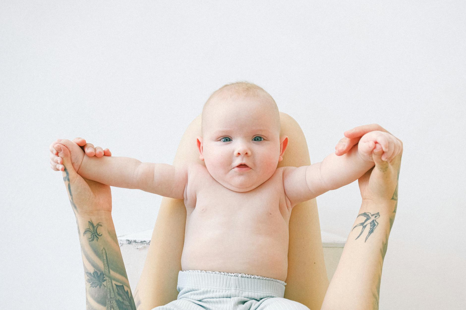 unrecognizable woman holding baby by hands on knees in light bedroom