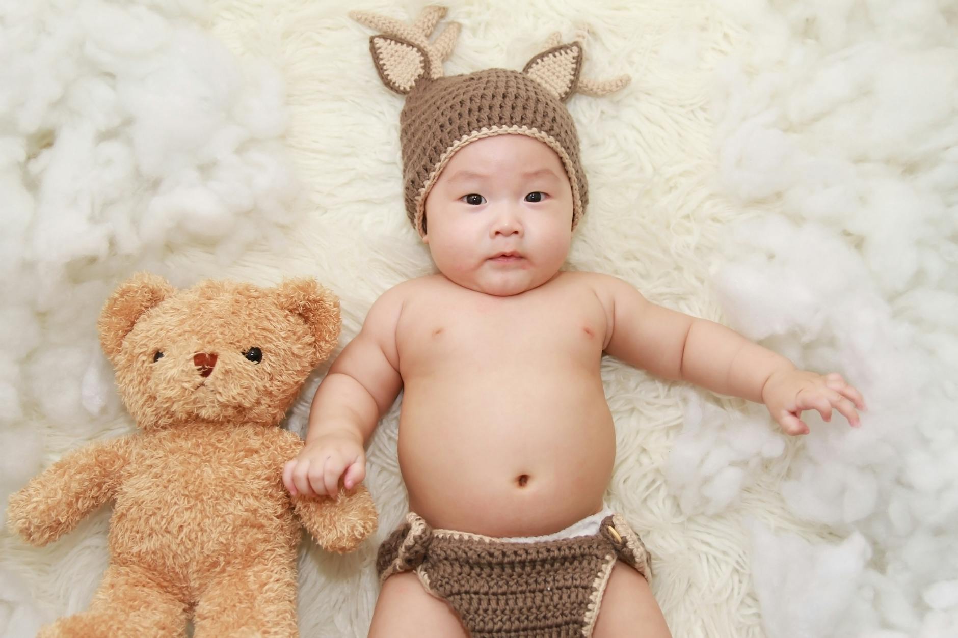 baby lying on white cushion beside brown bear plush toy