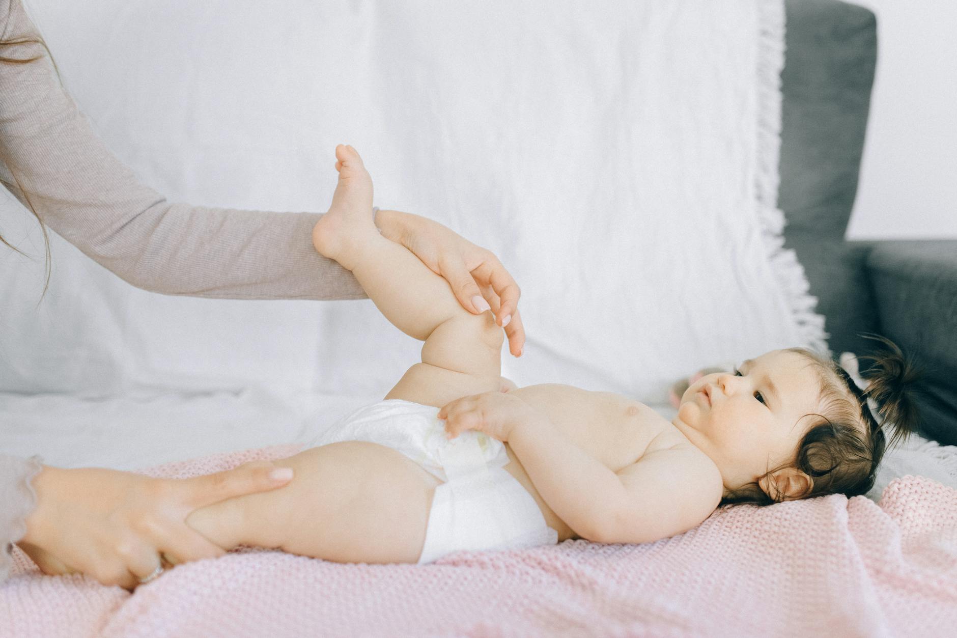 baby in white diaper lying on bed