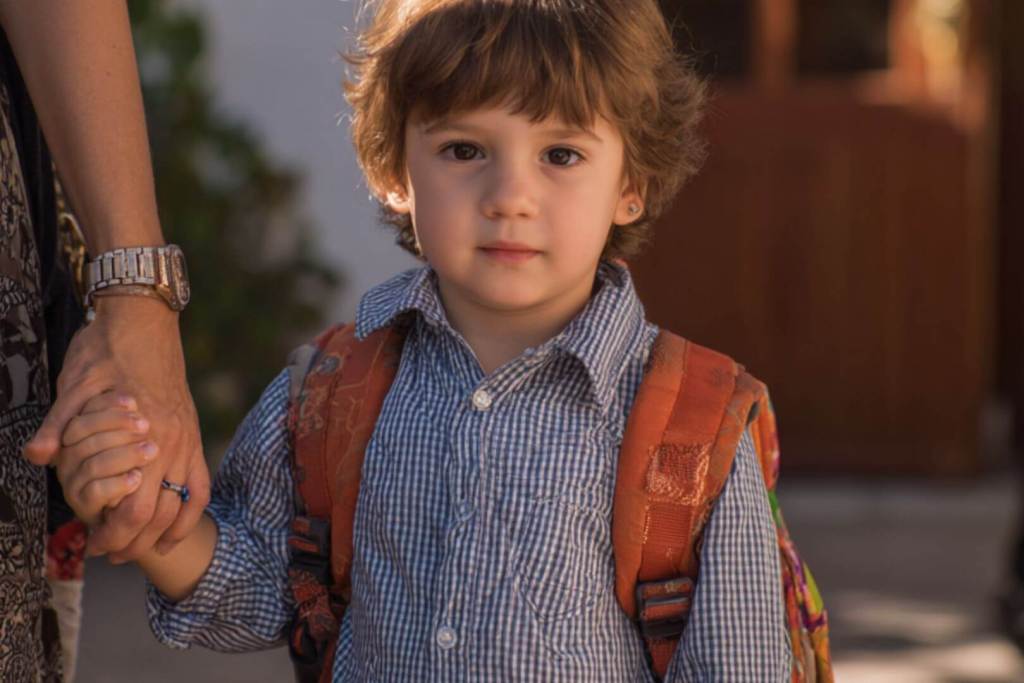 Niño con mochila agarrado de la mano de su madre en la entrada del colegio.