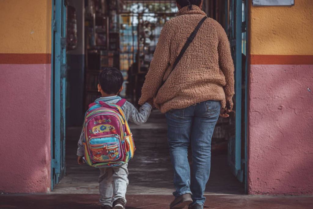 Niño con mochila colorida caminando con su madre hacia la puerta del colegio.