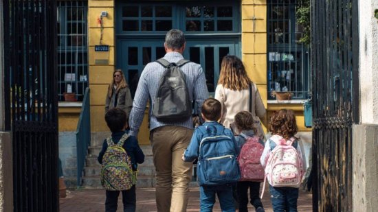 Familia entrando al colegio con niños pequeños y mochilas en la vuelta al cole.