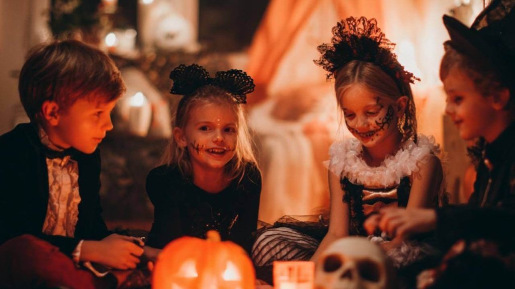 Niños disfrazados celebrando Halloween alrededor de una calabaza iluminada y decoraciones terroríficas.