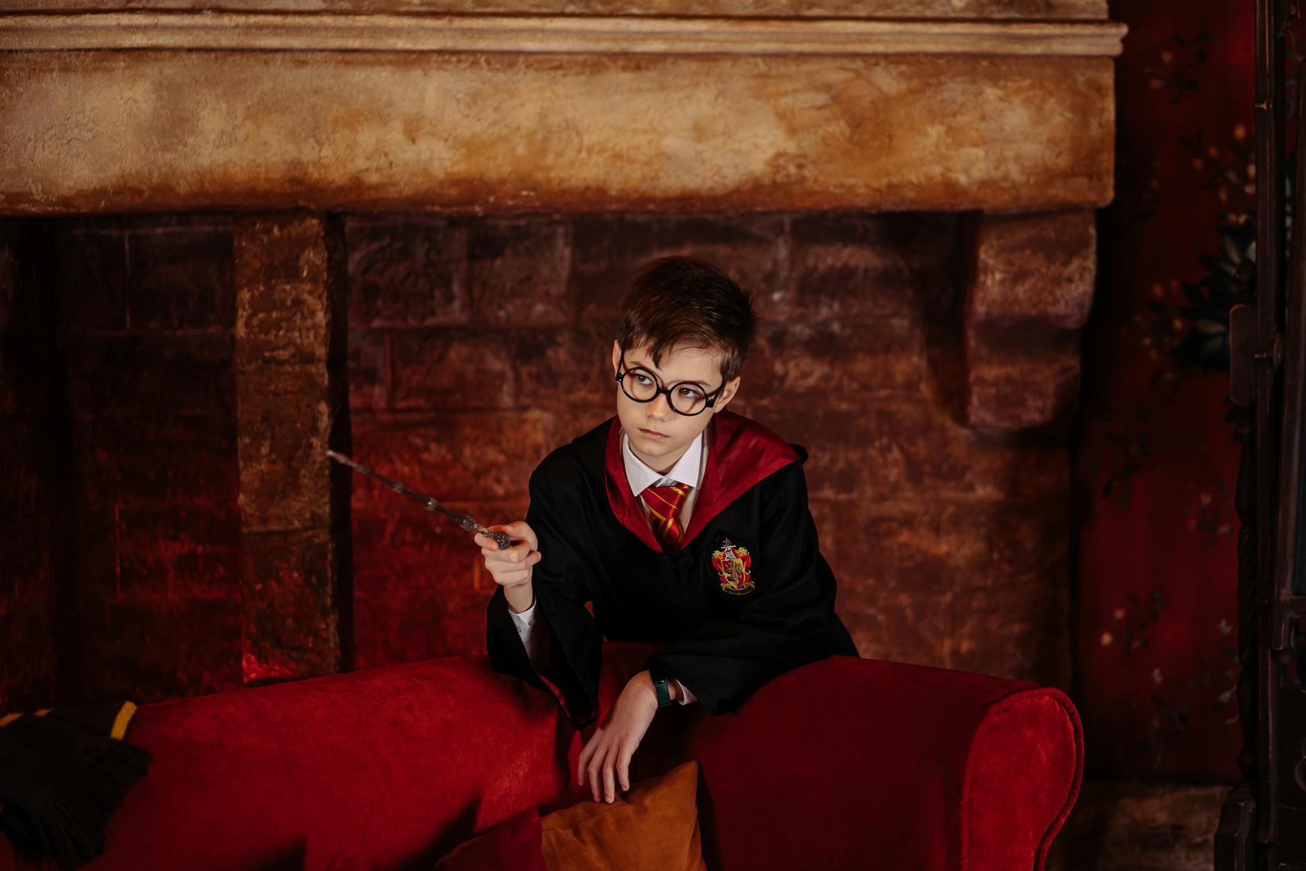 a boy wearing a black robe holding a wooden stick near the sofa