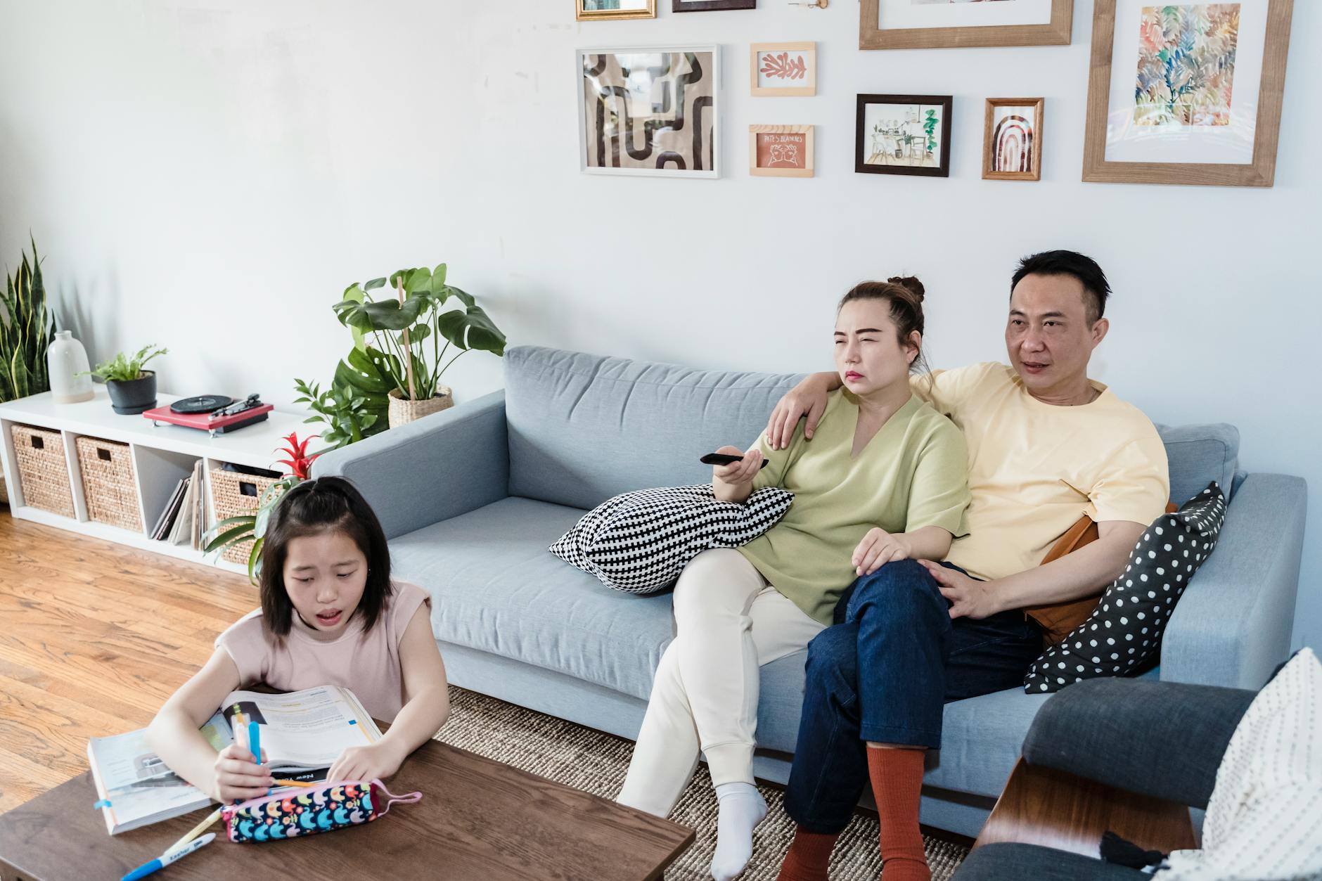 a girl doing her homework beside her parents in a living room
