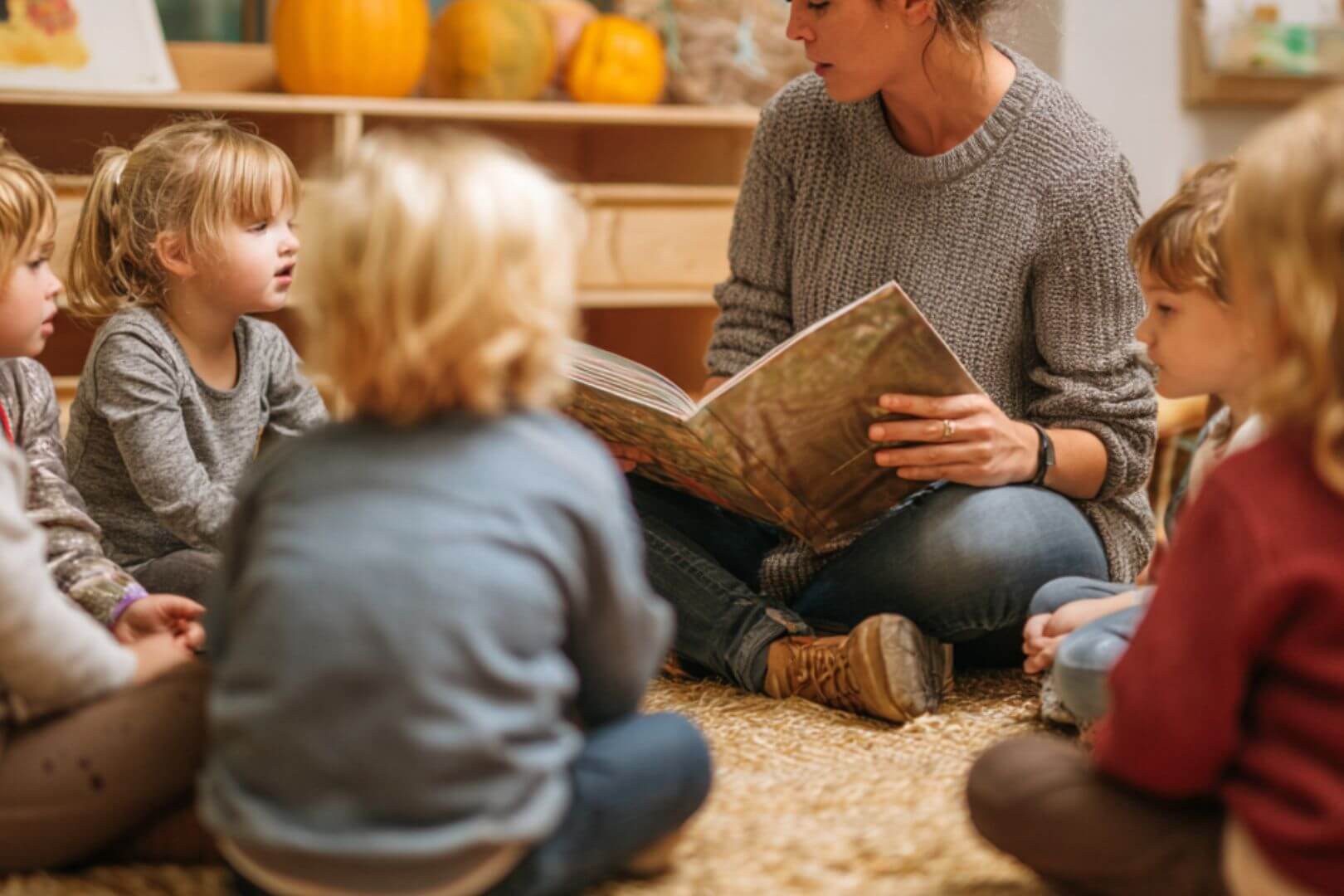 Maestra rodeada de niños en círculo mientras lee un libro en el aula de infantil.