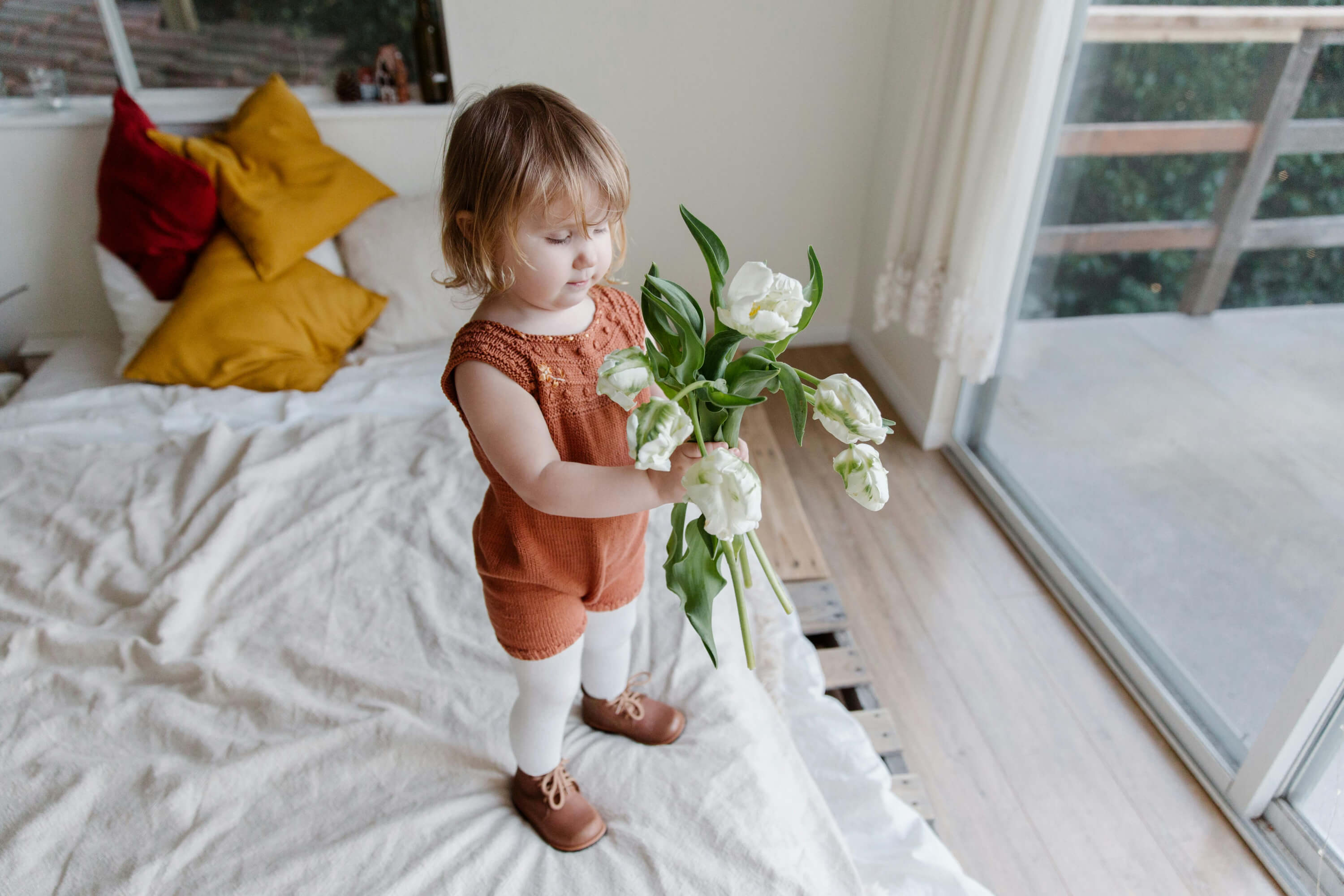 Niña pequeña con flores sobre la cama