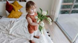 Niña pequeña con flores sobre la cama