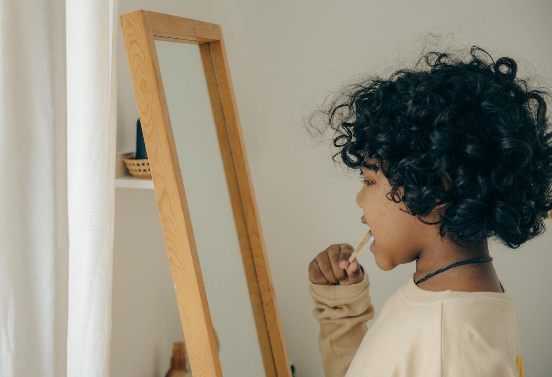 ethnic kid brushing teeth opposite mirror