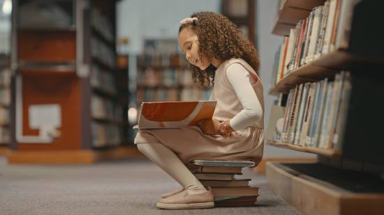 Una niña, leyendo en la biblioteca