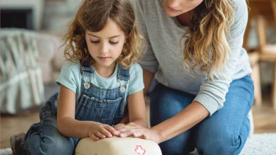 Niña aprendiendo maniobras de reanimación cardiopulmonar con la guía de su madre en casa.