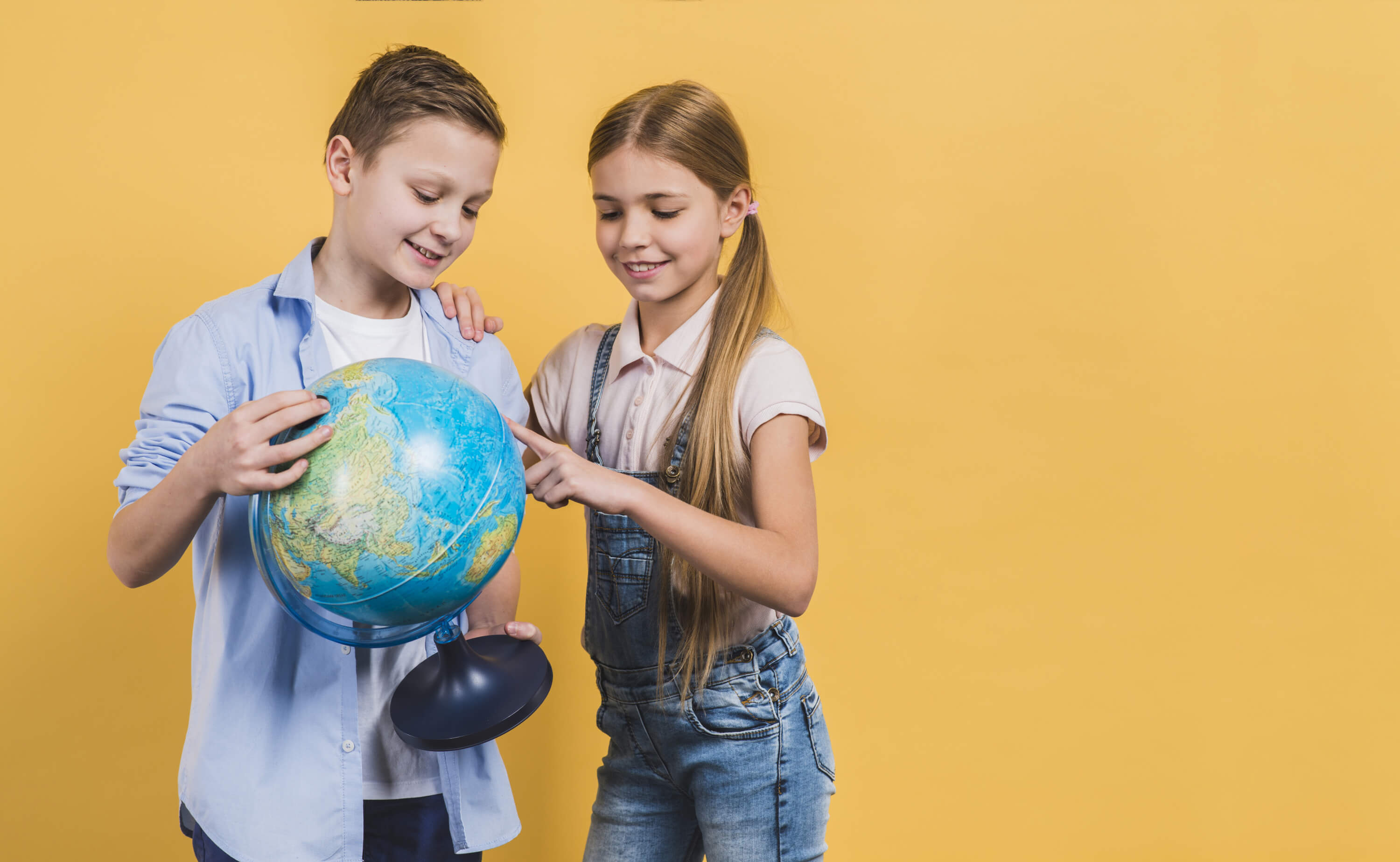 girl-pointing-globe-hold-by-his-friend-against-yellow-background