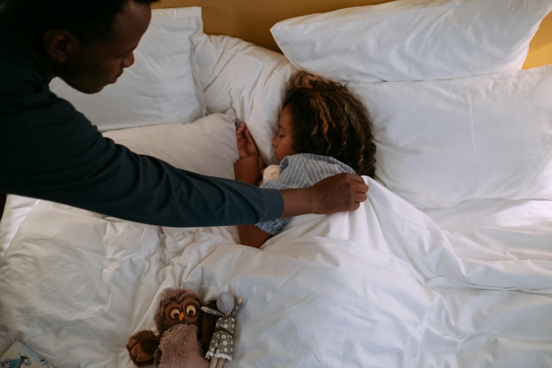 a man fixing a blanket on a girl sleeping in bed