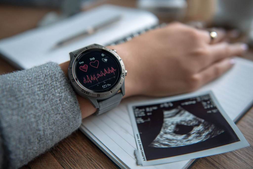 Primer plano de un smartwatch con datos de sueño junto a una ecografía: la tecnología y la maternidad se unen para cuidar mejor el embarazo desde casa.