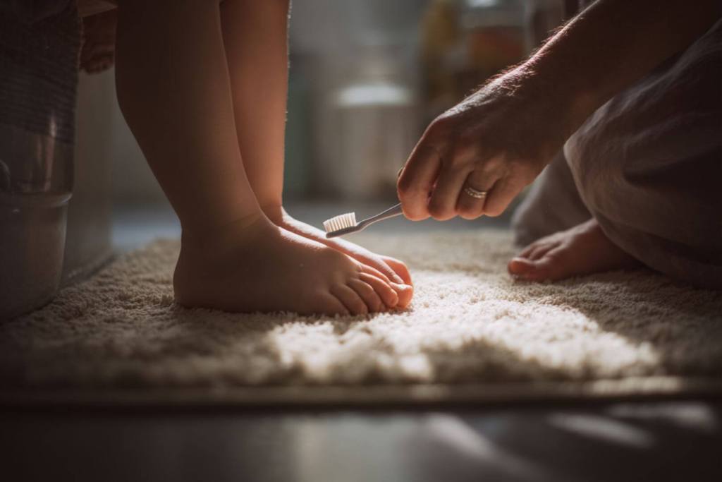 Luz tenue y ambiente íntimo mientras un adulto cuida la higiene de los pies de un niño.