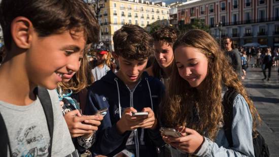 Un grupo de adolescentes españoles consultando sus teléfonos móviles en una plaza urbana.