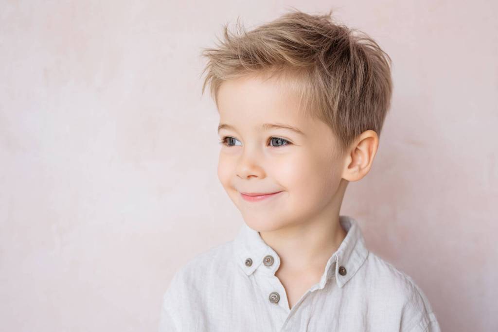 Niño pequeño rubio sonriente con camisa blanca y fondo rosa claro