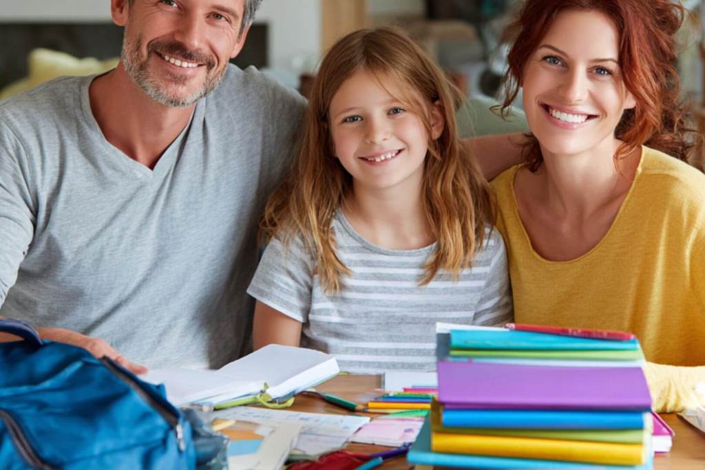 Padres e hija sonrientes organizando los libros y cuadernos para el nuevo curso escolar.