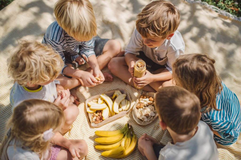 Grupo de niños compartiendo bananas y frutos secos durante un picnic.