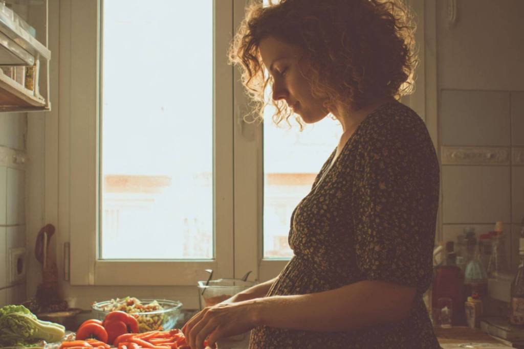 Mujer embarazada cortando verduras en la cocina, símbolo de alimentación equilibrada y saludable en el embarazo.