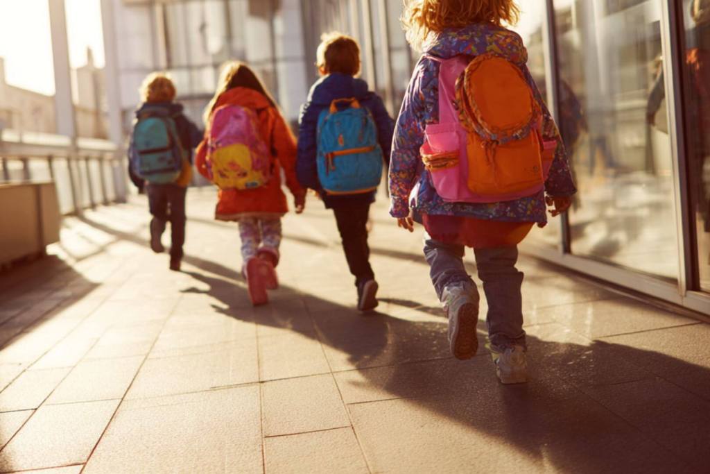 grupo de niños caminando hacia la escuela con mochilas de colores, vuelta al cole.
