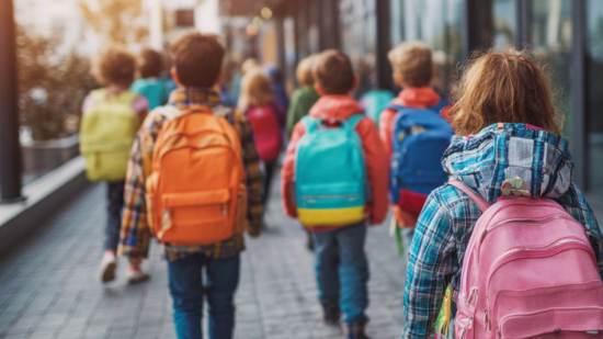 fila de niños con mochilas de colores dirigiéndose al colegio en la vuelta al cole.