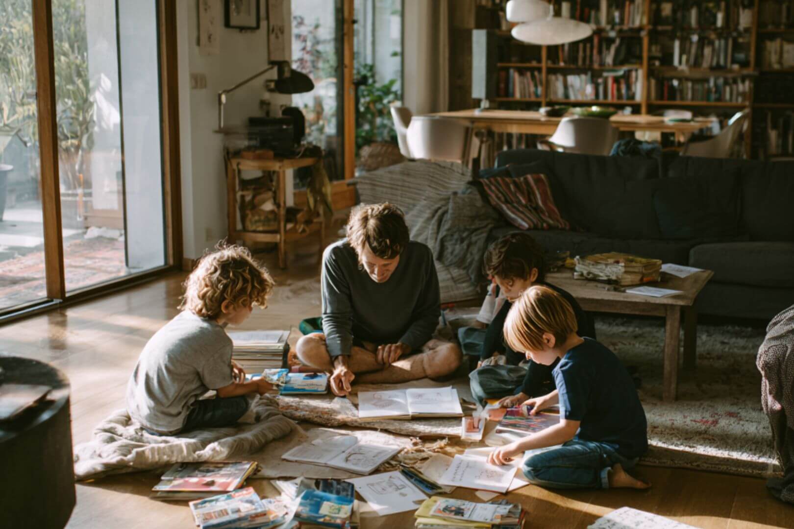 Familia con niños de diferentes edades leyendo juntos en casa, rodeados de libros y juegos, en un espacio acogedor y luminoso.