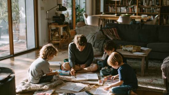 Familia con niños de diferentes edades leyendo juntos en casa, rodeados de libros y juegos, en un espacio acogedor y luminoso.