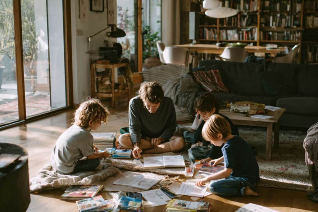 Familia con niños de diferentes edades leyendo juntos en casa, rodeados de libros y juegos, en un espacio acogedor y luminoso.