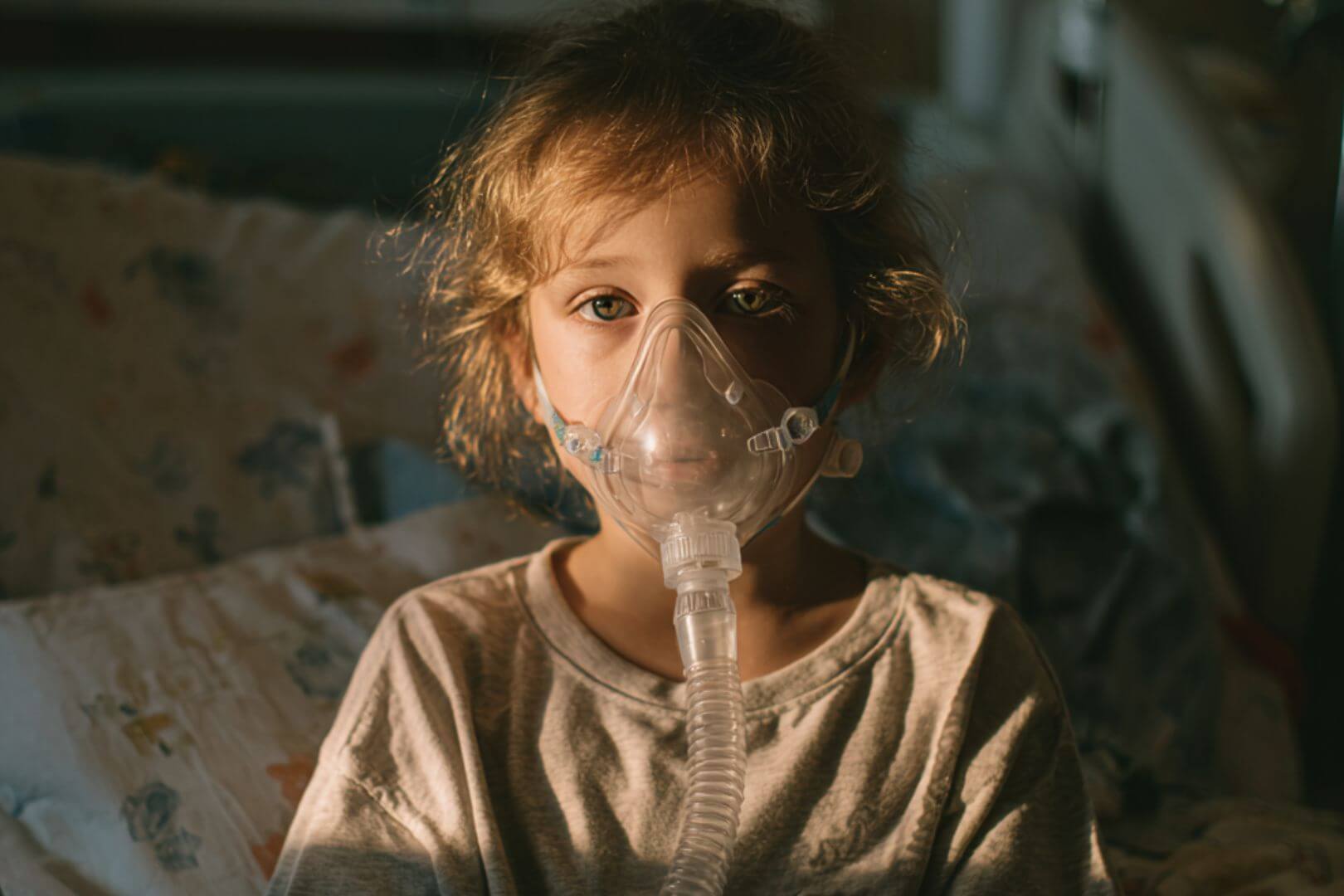 Niña con mascarilla de oxígeno en la cama, en tratamiento por asma, símbolo de la atención y cuidados necesarios en la infancia.