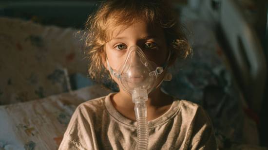 Niña con mascarilla de oxígeno en la cama, en tratamiento por asma, símbolo de la atención y cuidados necesarios en la infancia.
