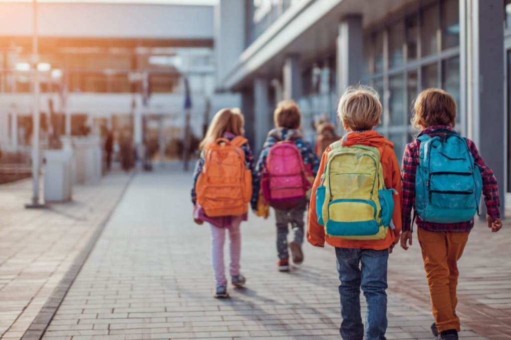 Grupo de niños pequeños con mochilas de colores entrando al colegio al inicio de curso.